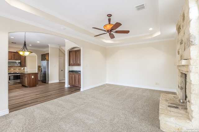 unfurnished living room featuring dark wood-type flooring, ceiling fan, a tray ceiling, and ornamental molding