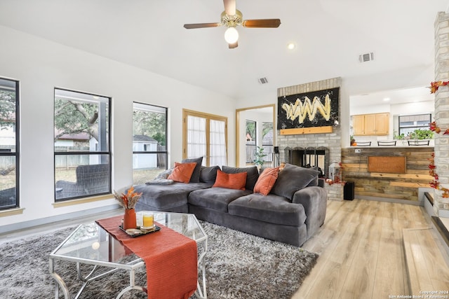 living room with ceiling fan, vaulted ceiling, a brick fireplace, and light hardwood / wood-style flooring