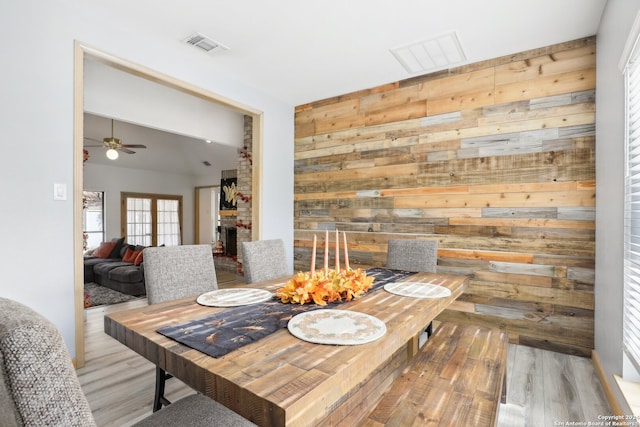 dining area featuring wooden walls, a brick fireplace, ceiling fan, and light hardwood / wood-style flooring