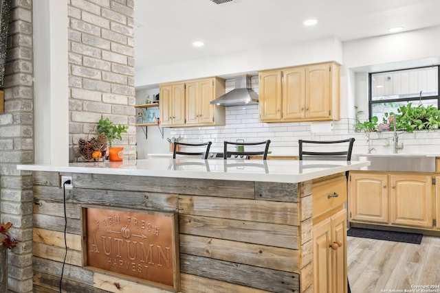 kitchen featuring light brown cabinets, decorative backsplash, light hardwood / wood-style flooring, and wall chimney range hood