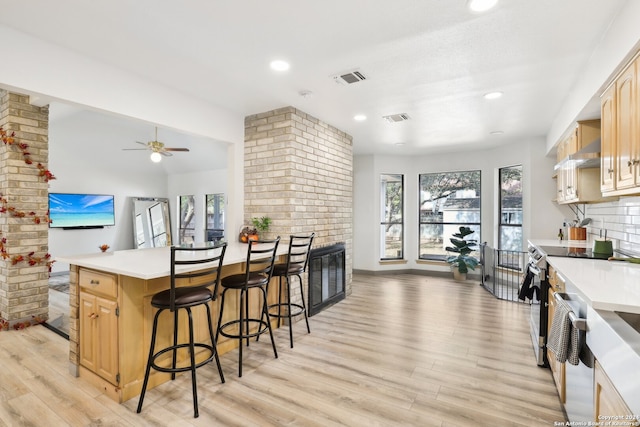 kitchen featuring a kitchen bar, light brown cabinets, light hardwood / wood-style floors, electric range, and ceiling fan