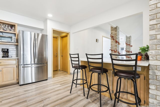 kitchen featuring light brown cabinetry, a kitchen bar, stainless steel fridge, and light hardwood / wood-style flooring