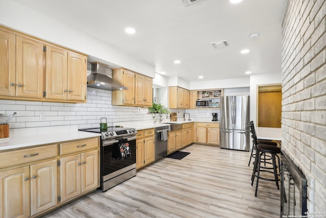 kitchen with sink, appliances with stainless steel finishes, tasteful backsplash, wall chimney exhaust hood, and light hardwood / wood-style flooring