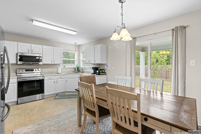 kitchen featuring white cabinets, appliances with stainless steel finishes, a chandelier, and decorative light fixtures