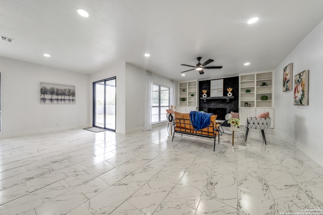 living room featuring a brick fireplace, built in features, a textured ceiling, and ceiling fan