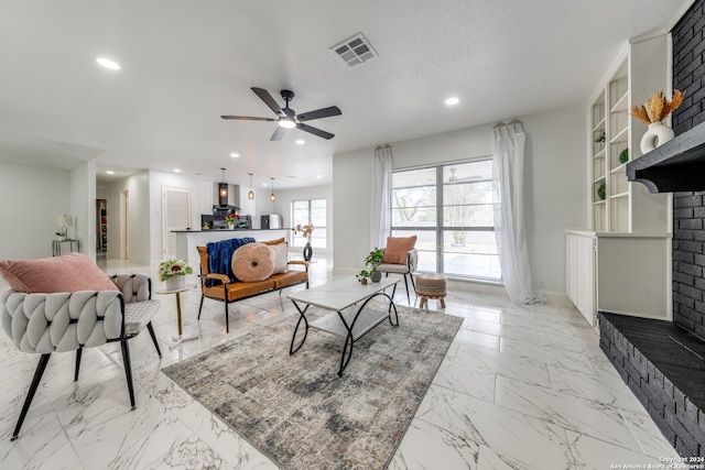 living room with a brick fireplace, built in features, a textured ceiling, and ceiling fan