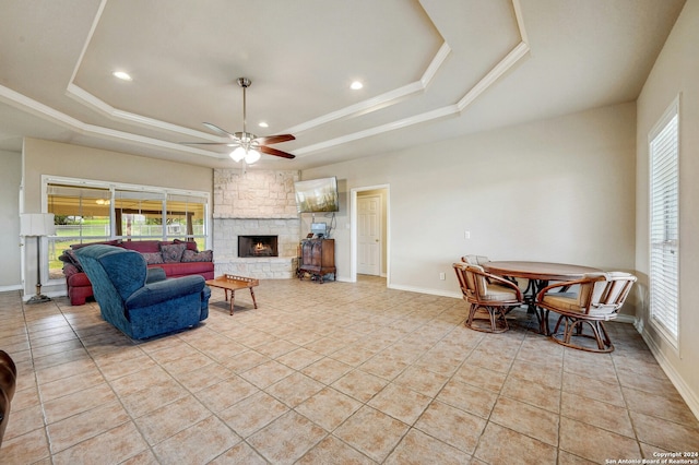 living room with ceiling fan, light tile patterned flooring, a stone fireplace, and a tray ceiling