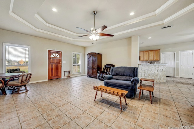 tiled living room with ceiling fan, a wealth of natural light, and a tray ceiling