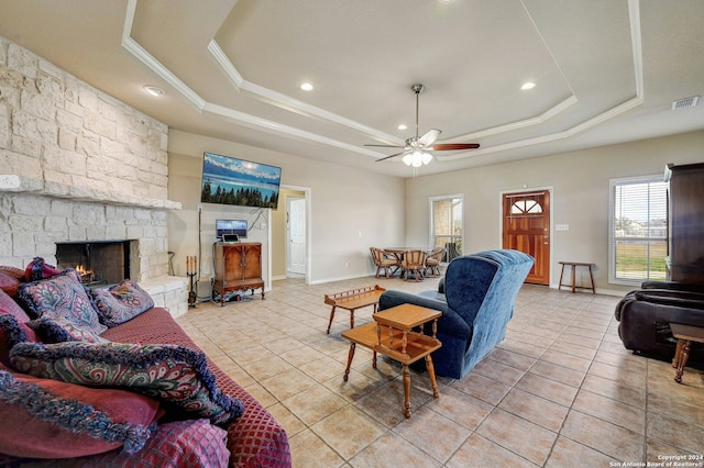 living room featuring ceiling fan, a stone fireplace, a raised ceiling, and light tile patterned floors