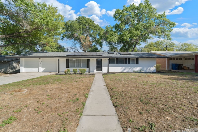 ranch-style home with a front lawn, a garage, and solar panels