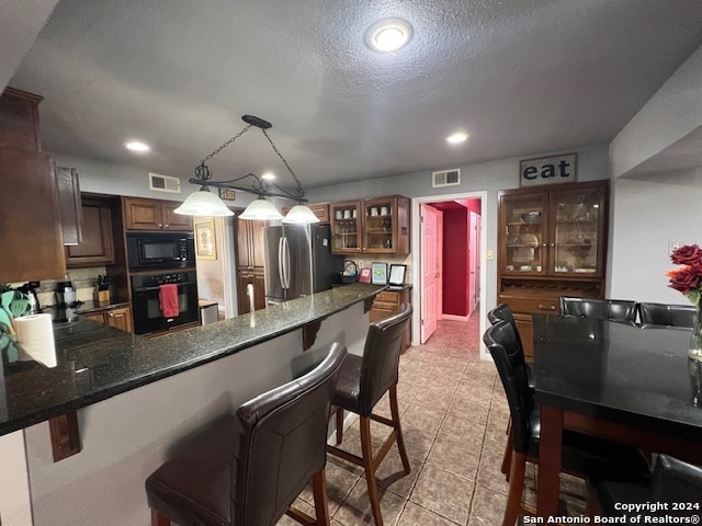 kitchen featuring a breakfast bar, black appliances, kitchen peninsula, a textured ceiling, and hanging light fixtures