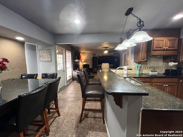 kitchen with a breakfast bar area, tasteful backsplash, sink, ceiling fan, and pendant lighting