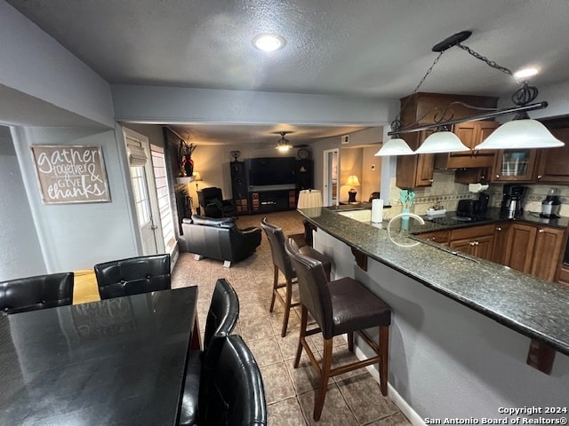 kitchen featuring hanging light fixtures, light tile patterned flooring, a breakfast bar, backsplash, and dark stone countertops