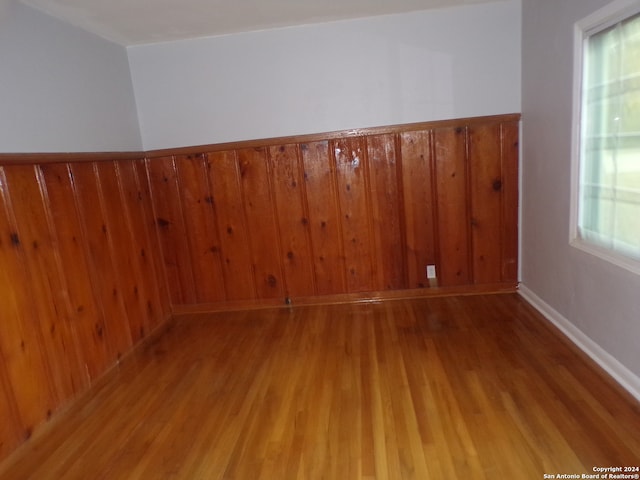 unfurnished room featuring wooden walls, wood-type flooring, and plenty of natural light