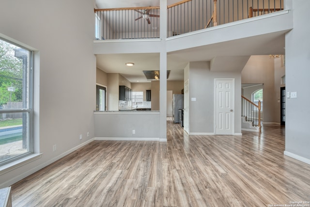 unfurnished living room featuring a high ceiling, ceiling fan, a healthy amount of sunlight, and light hardwood / wood-style floors