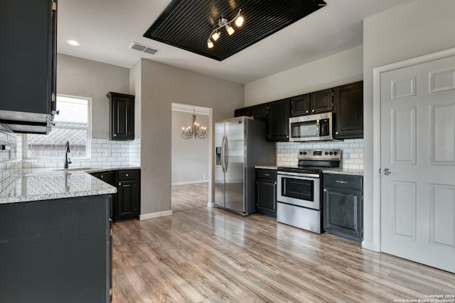 kitchen with sink, backsplash, light stone countertops, light wood-type flooring, and appliances with stainless steel finishes