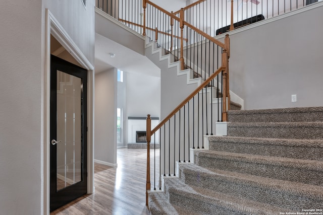 stairs with hardwood / wood-style floors, a towering ceiling, and a tile fireplace