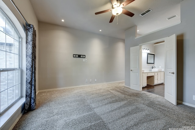 unfurnished bedroom featuring ensuite bath, ceiling fan, and dark carpet