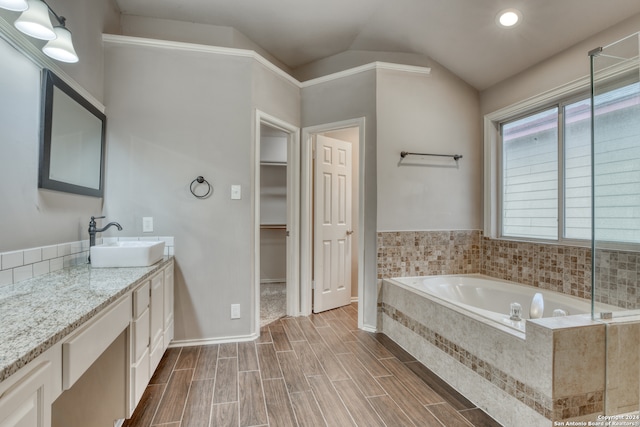 bathroom featuring vanity, vaulted ceiling, and tiled tub