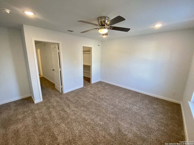 unfurnished bedroom featuring a closet, a spacious closet, ceiling fan, and carpet floors