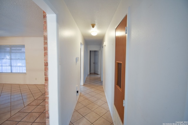 corridor featuring a textured ceiling and light tile patterned floors