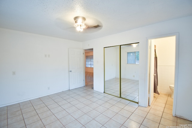 unfurnished bedroom featuring tile walls, light tile patterned floors, ensuite bathroom, ceiling fan, and a closet