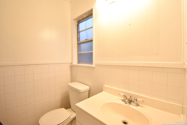 bathroom featuring toilet, vanity, and tile walls