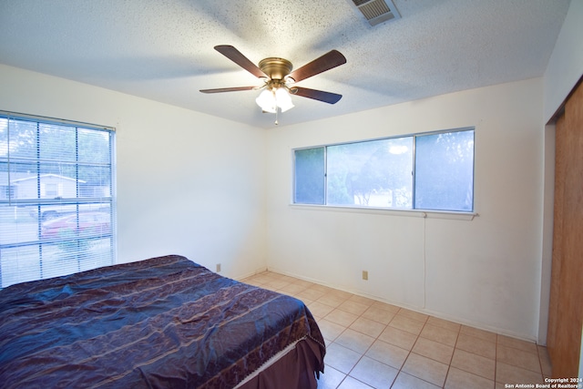 tiled bedroom with ceiling fan and a textured ceiling