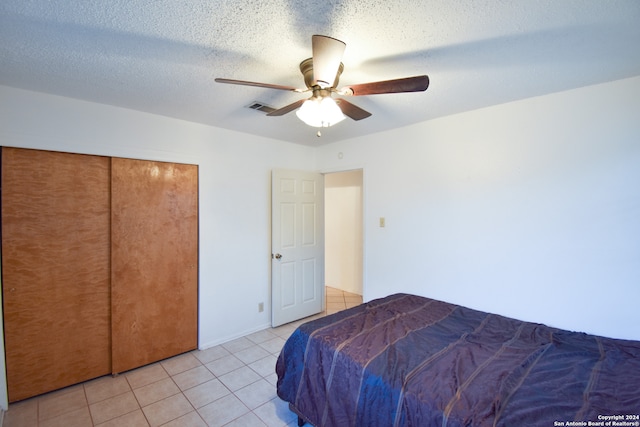 bedroom with light tile patterned floors, ceiling fan, a textured ceiling, and a closet