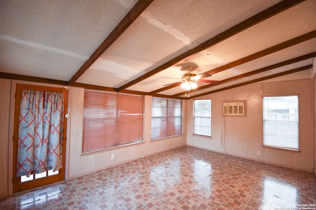 empty room featuring wood walls, ceiling fan, a textured ceiling, and lofted ceiling with beams