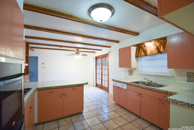 kitchen featuring light tile patterned flooring, beamed ceiling, sink, kitchen peninsula, and oven