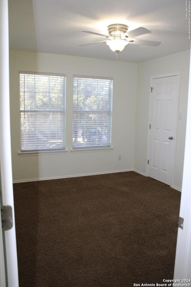 empty room featuring ceiling fan and dark carpet