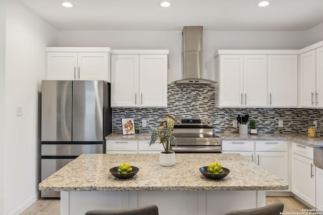 kitchen with a kitchen breakfast bar, wall chimney range hood, white cabinetry, and appliances with stainless steel finishes