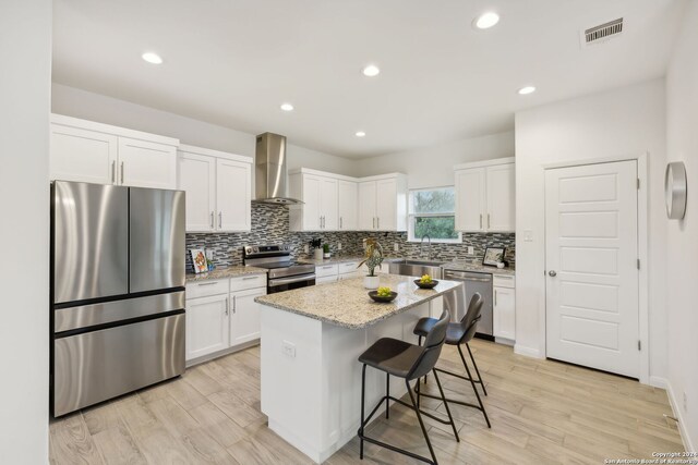 kitchen with light stone counters, light wood-type flooring, appliances with stainless steel finishes, wall chimney exhaust hood, and a center island