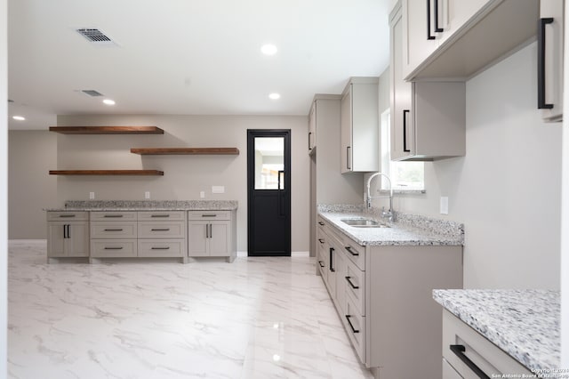 kitchen with gray cabinets, light stone countertops, and sink