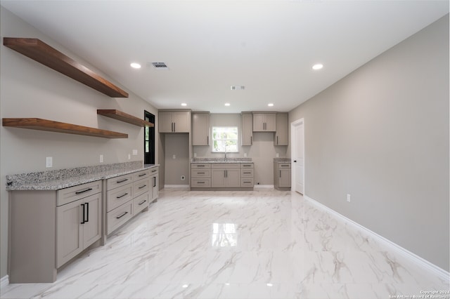 kitchen with light stone countertops, gray cabinetry, and sink