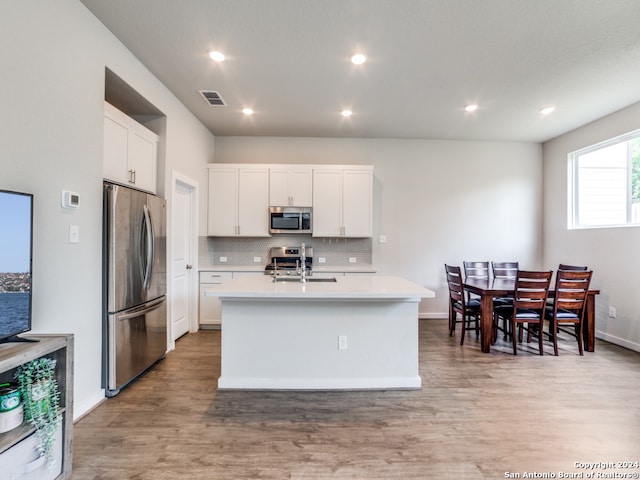 kitchen with white cabinets, light hardwood / wood-style floors, stainless steel appliances, and a center island with sink