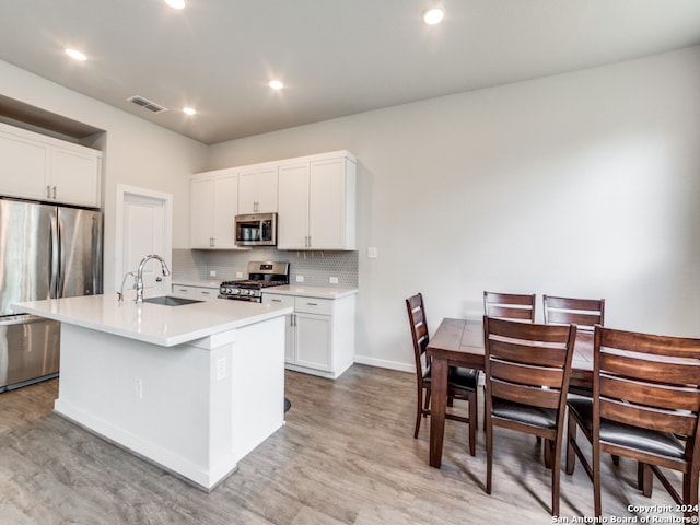 kitchen featuring stainless steel appliances, white cabinetry, sink, an island with sink, and light hardwood / wood-style floors