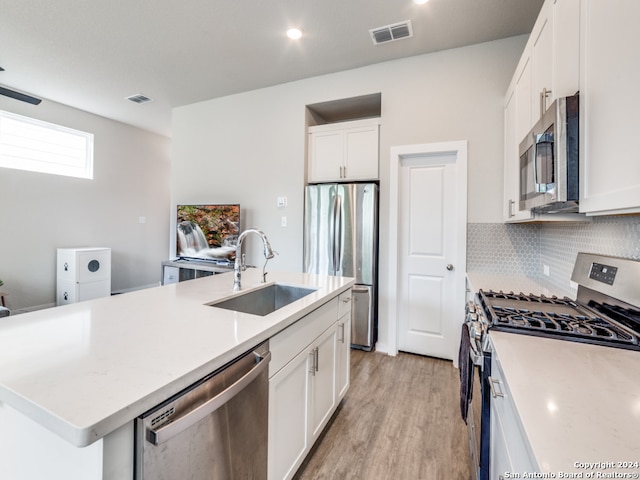 kitchen with stainless steel appliances, white cabinetry, sink, light hardwood / wood-style floors, and a kitchen island with sink