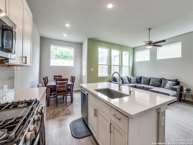 kitchen with white cabinets, light hardwood / wood-style flooring, sink, an island with sink, and appliances with stainless steel finishes