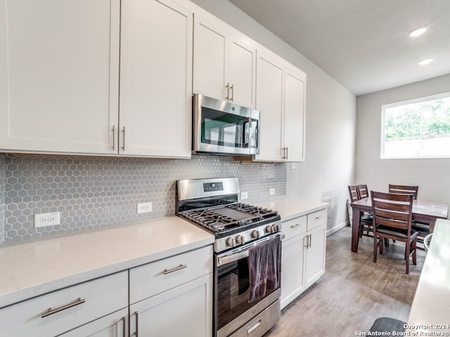 kitchen with white cabinets, light wood-type flooring, stainless steel appliances, and decorative backsplash