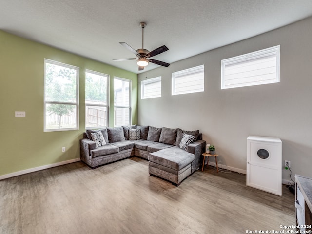 living room with ceiling fan, a textured ceiling, and light wood-type flooring