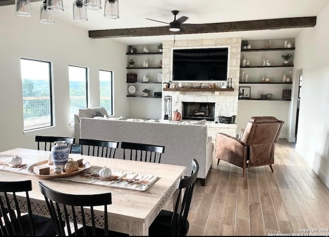 dining space featuring a stone fireplace, beam ceiling, ceiling fan, and light hardwood / wood-style flooring