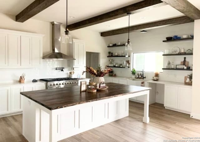 kitchen featuring a kitchen island, decorative light fixtures, wood counters, white cabinets, and wall chimney exhaust hood