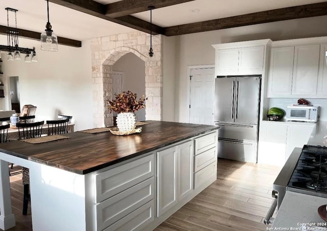 kitchen featuring butcher block counters, appliances with stainless steel finishes, beam ceiling, white cabinets, and a center island