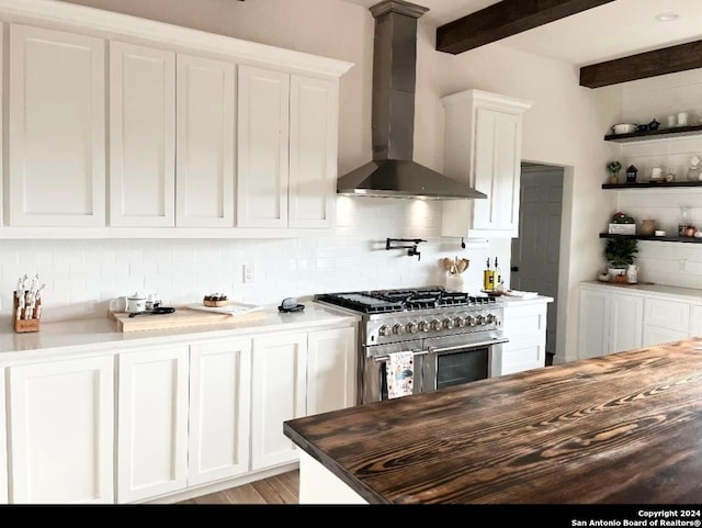 kitchen featuring high end stainless steel range oven, white cabinetry, wall chimney range hood, and butcher block counters