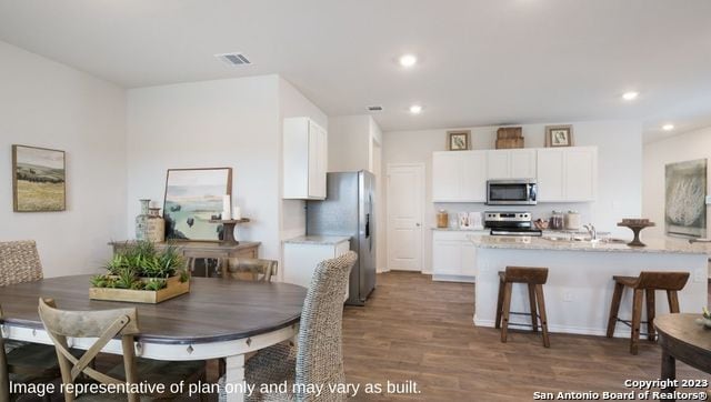 kitchen with light stone counters, stainless steel appliances, white cabinetry, a breakfast bar, and dark wood-type flooring