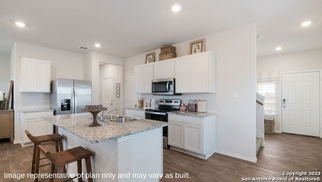 kitchen with stainless steel appliances, light stone counters, a kitchen island with sink, dark hardwood / wood-style floors, and white cabinetry