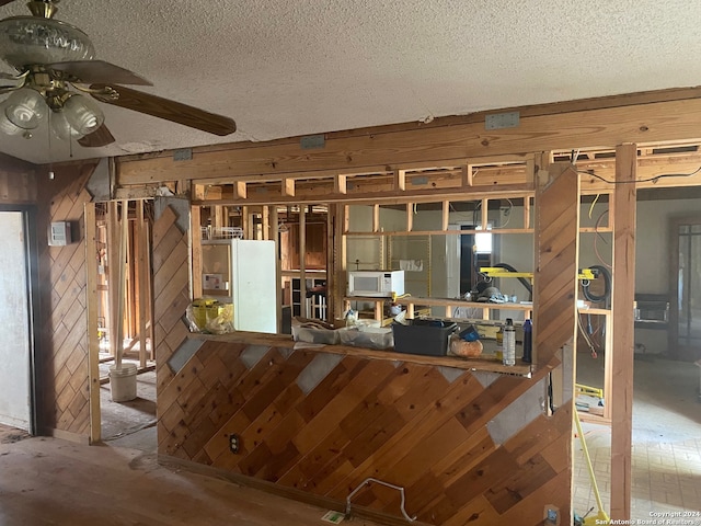 kitchen featuring wood walls, a textured ceiling, and ceiling fan