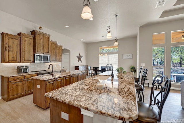 kitchen featuring an island with sink, decorative light fixtures, light stone counters, and light wood-type flooring